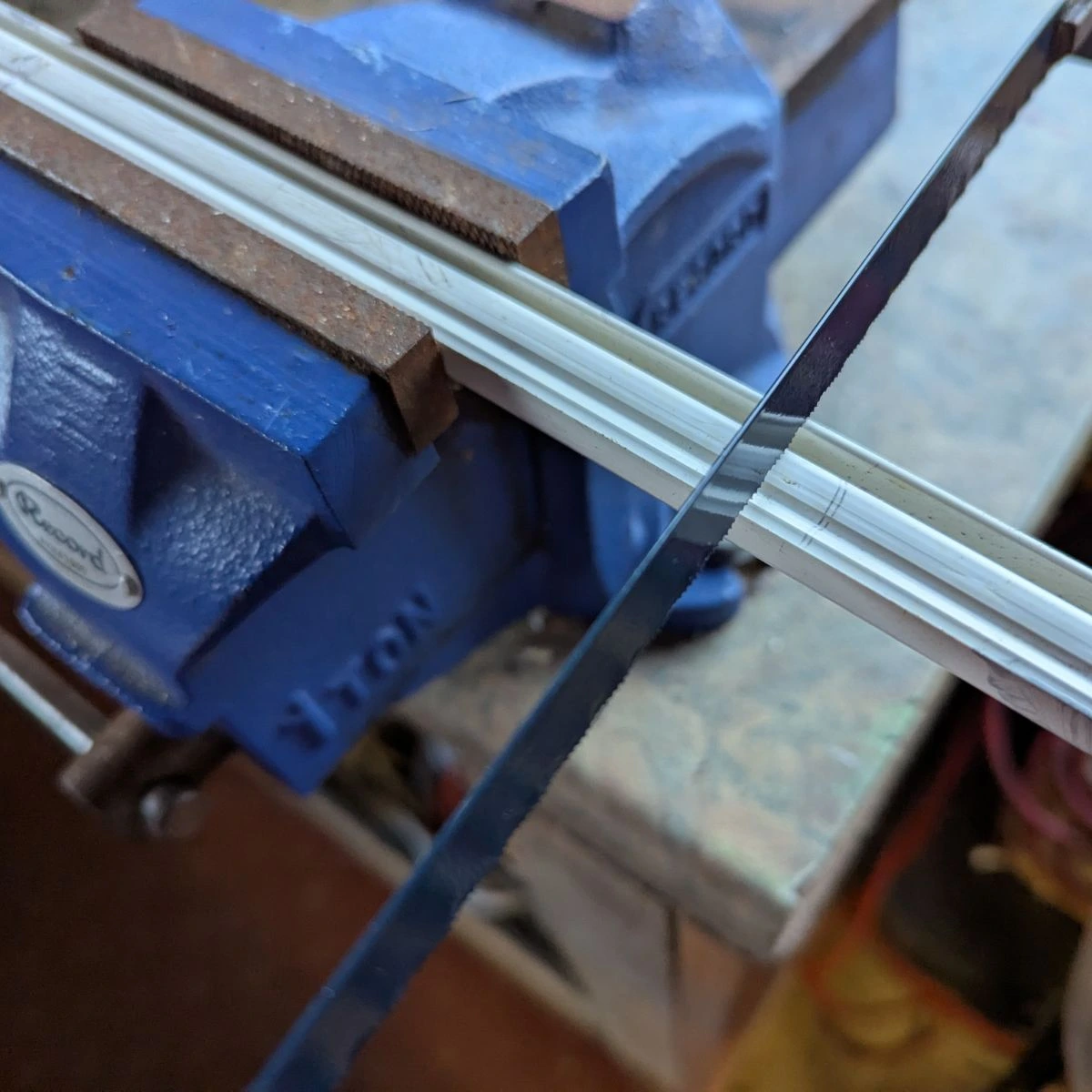 hacksaw cutting curtain rail held in a vice